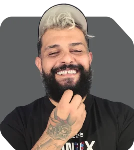 Instrutor de vários treinamentos, Jeferson é um homem de barba, boné e cabelo descolorido sorrindo com a mão no queixo.